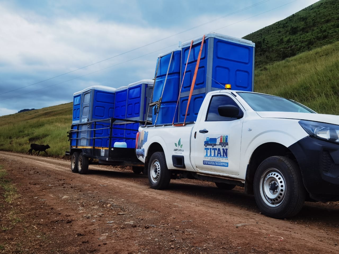Titan truck carrying blue portable toilets along a rural road